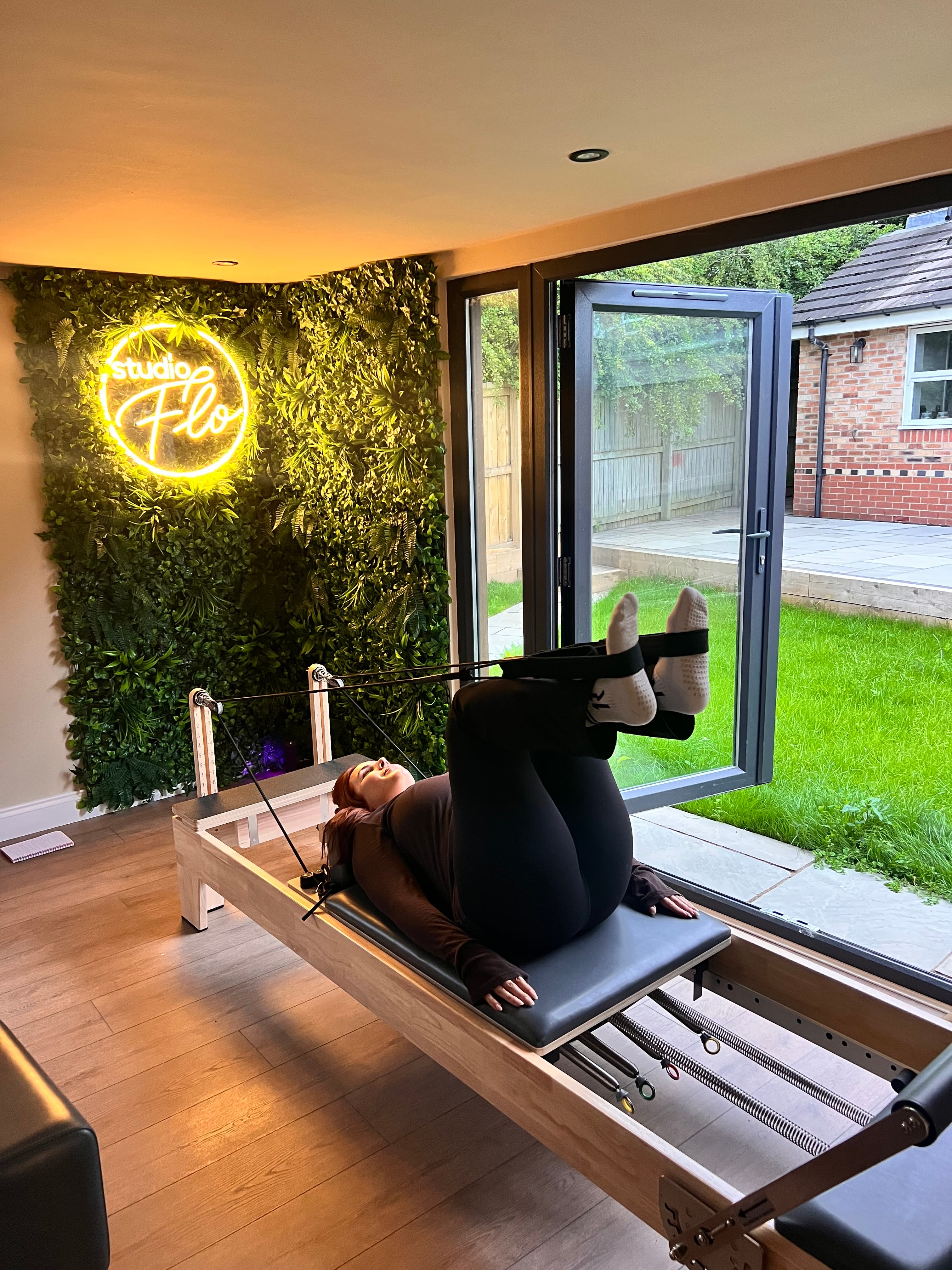 Reformer Pilates session at Studio Flo with neon sign and garden views